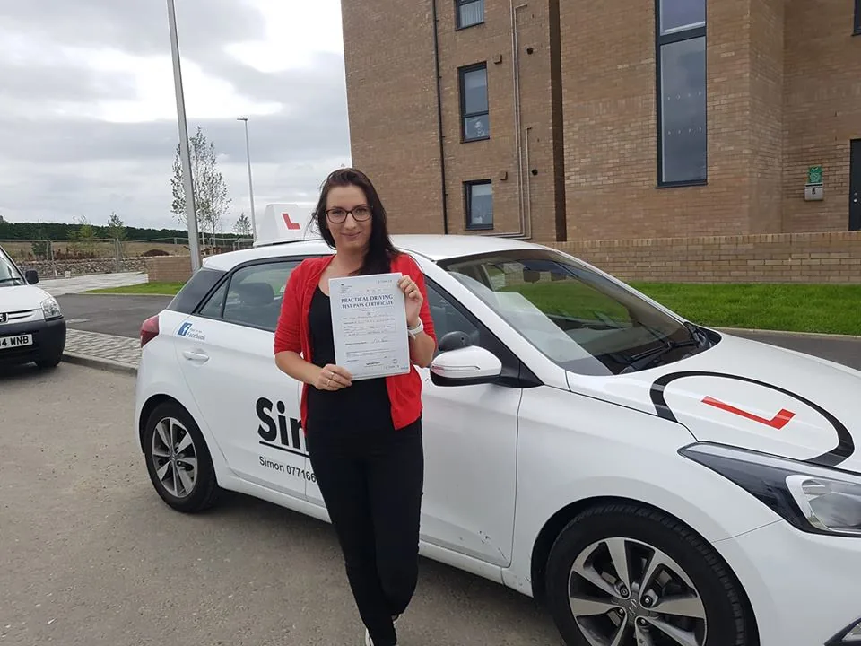 A successful learner holding their pass certificate beside a SimpL car